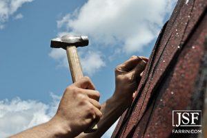 roofer hammering a nail into shingles