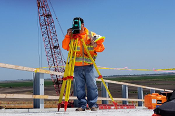 A construction worker in high vis gear surveying with a crane in the background.