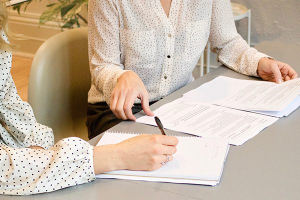 A white woman takes notes while another goes over paperwork.