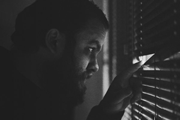 A suspicious man peeking through window blinds.