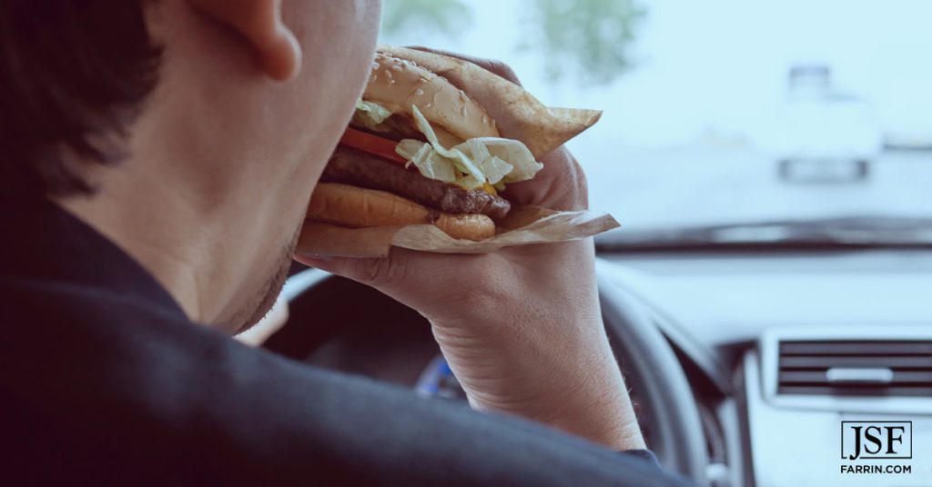 Driver eating a large burger while driving may increase his chances of a wreck.