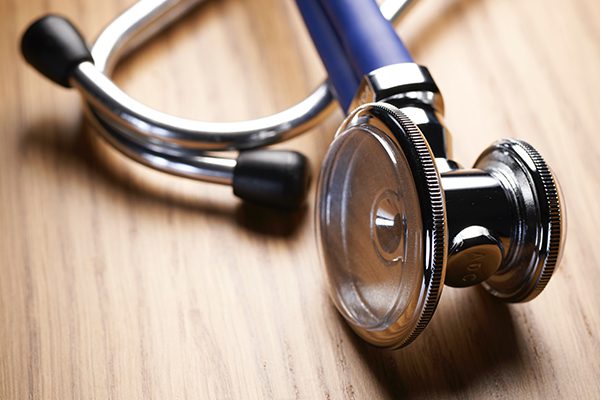 Close up of a silver doctor's stethoscope on a wooden desk.