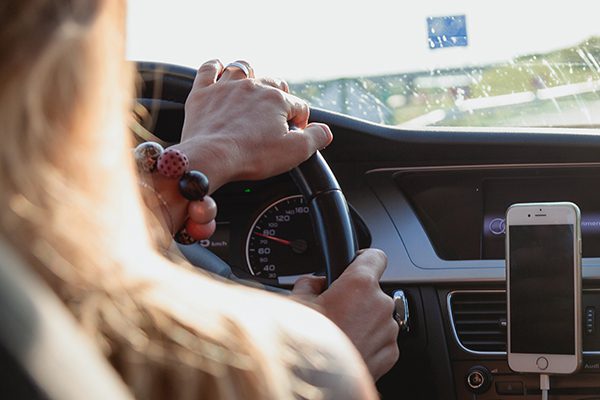 Young teen woman driving a car with a phone on the dashboard.
