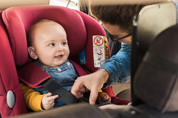 An infant being buckled into a carseat by their father.
