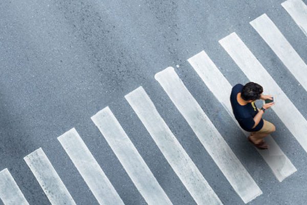 Aerial view of a man walking across a crosswalk but distracted by his cell phone.