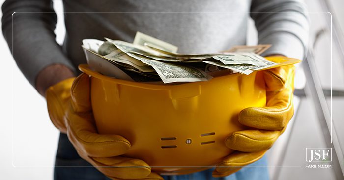 A worker holding a yellow hard hat filled with cash from his workers' compensation settlement.