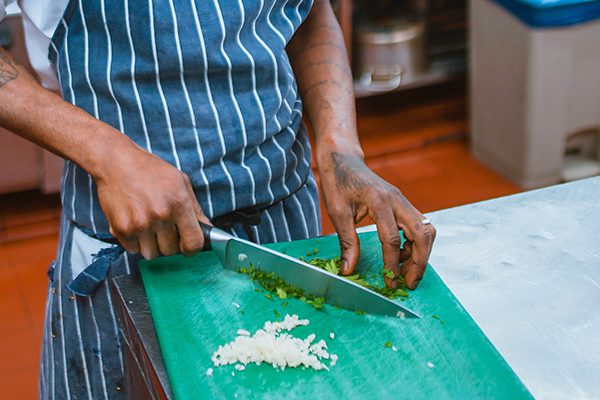 Restaurant chef chopping up herbs in the kitchen with a large knife.