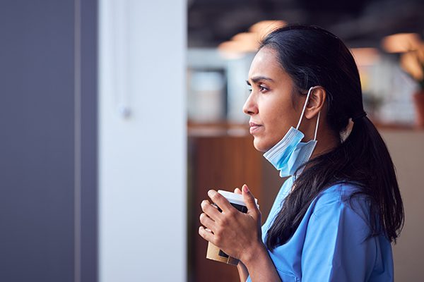 Female nurse on break with mask pulled down, drinking coffee.
