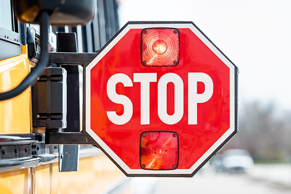 Blinking extended stop sign on the side of a yellow school bus.