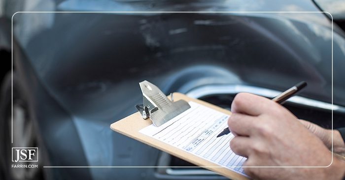 An insurance agent taking notes for a report on a damaged vehicle after a crash on a clipboard.