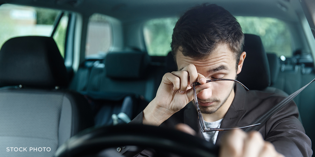 Drowsy driver rubbing his eyes, falling asleep at the wheel of his car.