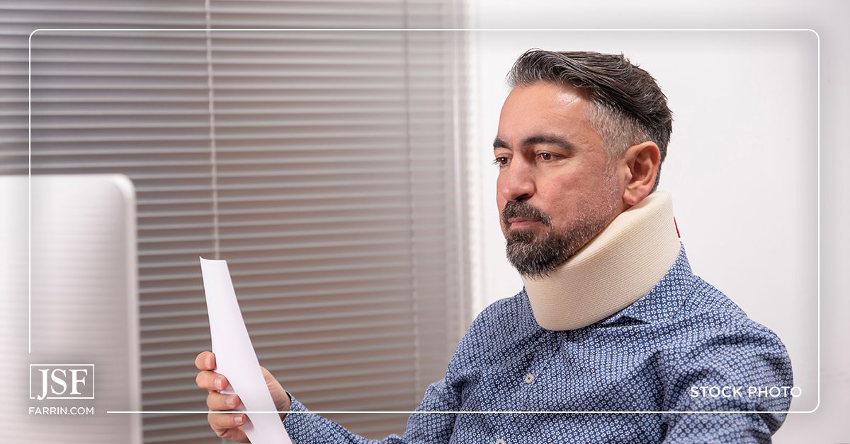 Concerned man in a neck brace sitting in front of a computer.