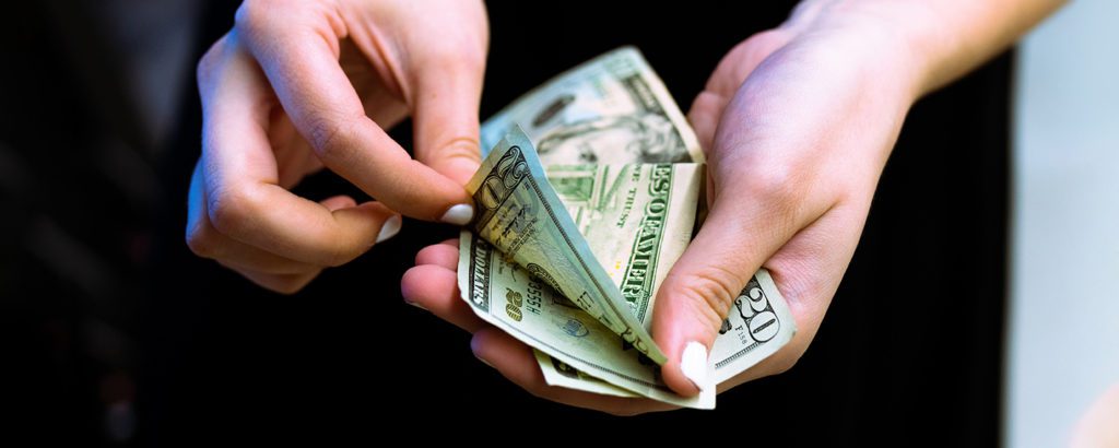 A woman going through twenty dollar bills in her hand.