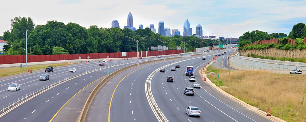 Aerial view of cars driving down a highway into Charlotte, NC, with the skyline in the distance.