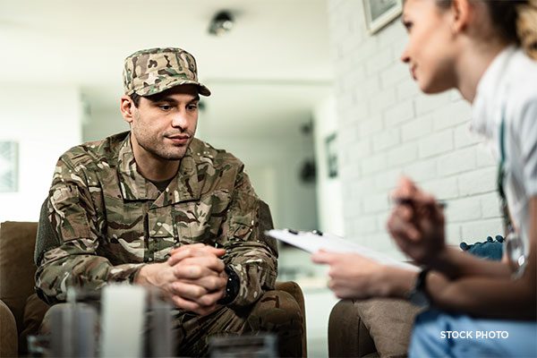Therapist fills out RFC form on clipboard while interviewing soldier in fatigues about his PTSD