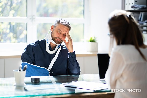 Law Offices of James Scott Farrin North Carolina auto accident lawyer consults with injured man showing neck & arm injuries.