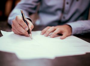 A man filling out insurance paperwork with a pen on a desk.