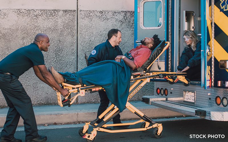 Paramedics loading an injured man on a stretcher into an ambulance.
