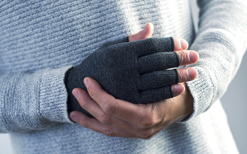 A person wearing a grey compression glove on their hand to relieve wrist pain.