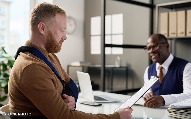 An injured client with his arm in a sling looking over paperwork with his attorney.