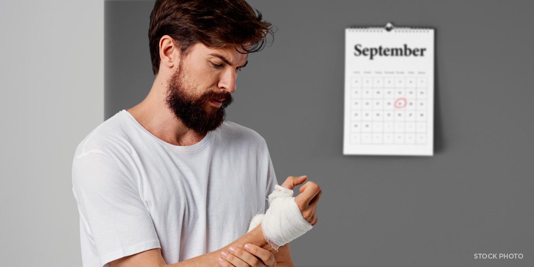A man looking at his injured hand, near a wall calendar with a deadline circled in red.