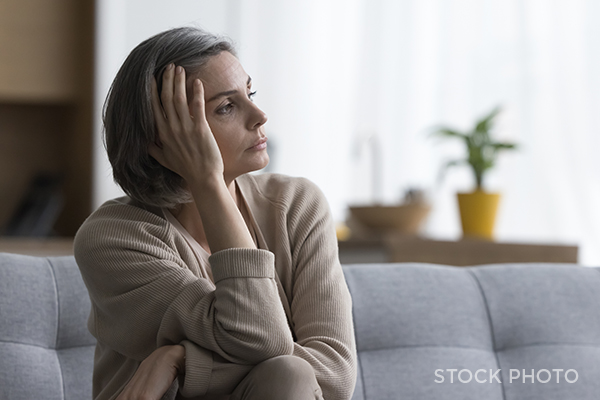 Upset woman on a grey couch looking off into the distance.