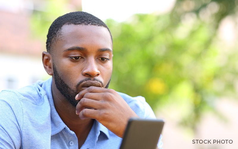 Black man looking regretfully with his hand on his chin at his phone.