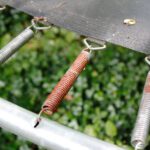 A rusted spring on an outdoor trampoline, creating a hazard.