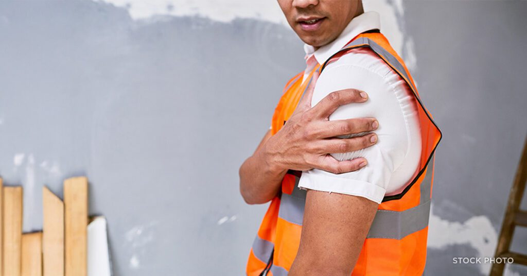 Law Offices of James Scott Farrin North Carolina workers’ compensation attorneys. Construction worker in safety vest holds injured shoulder at job site.