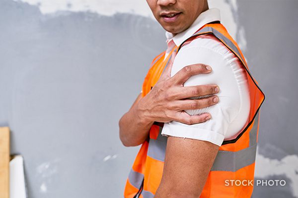 Law Offices of James Scott Farrin North Carolina workers’ compensation attorneys. Construction worker in safety vest holds injured shoulder at job site.