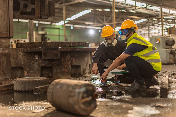 Law Offices of James Scott Farrin North Carolina workers’ compensation attorneys. Manufacturing workers wearing protective gear inspect hazardous spill on factory floor.